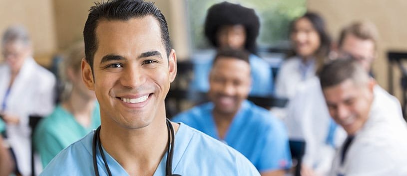 Male nurse smiling. In the background are other healthcare professionals.
